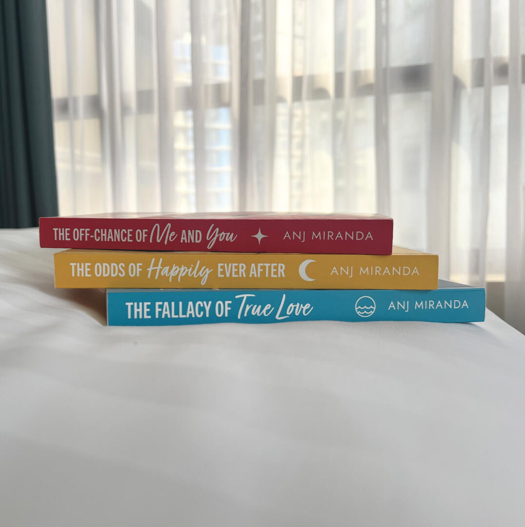 hand holding paperback books of the fallacy of true love, the odds of happily ever after, and the off-chance of me and you by anj miranda